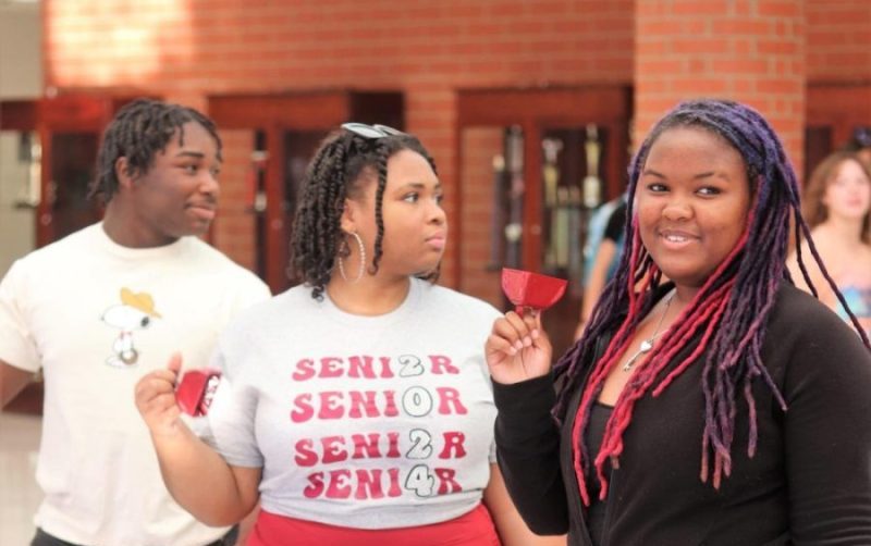 SGA members Standford Thompson (left), President Alivia Morris (center) and Nya Wright (right) greet students by ringing bells on the first half-day of school.